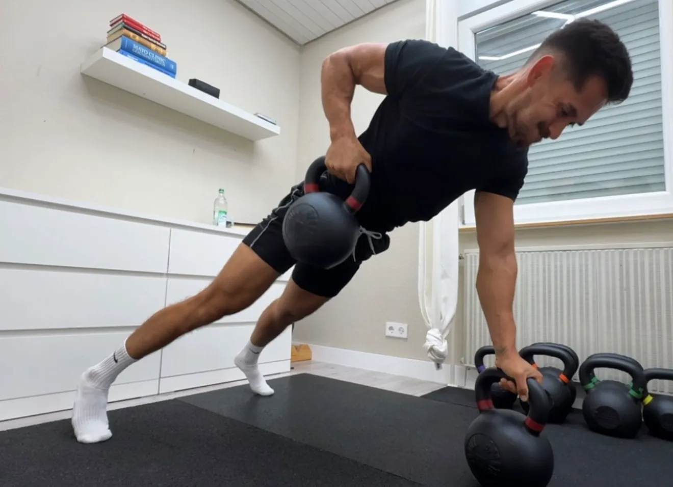 Eric Becker rudert zuhause mit einer Kettlebell, die andere Hand stützt sich auf einer zweiten Kettlebell ab